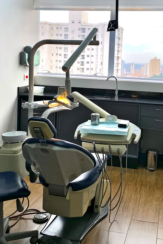 Sala clínica: a cadeira odontológica de estofado azul-marinho diante da janela com vista para a cidade.