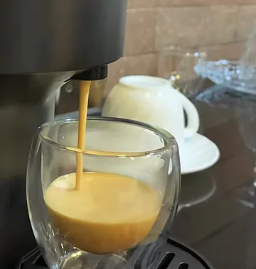 Café caindo numa xícara de vidro de parede dupla.