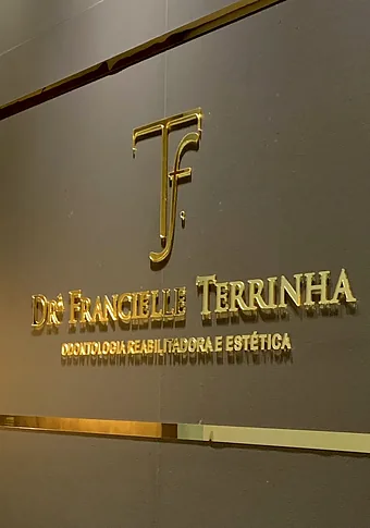 O nome Drª Francielle Terrinha, Odontologia Reabilitadora e Estética, em letras de metal na parede.