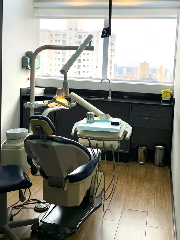 Sala clínica do consultório, com a cadeira e a janela para a cidade