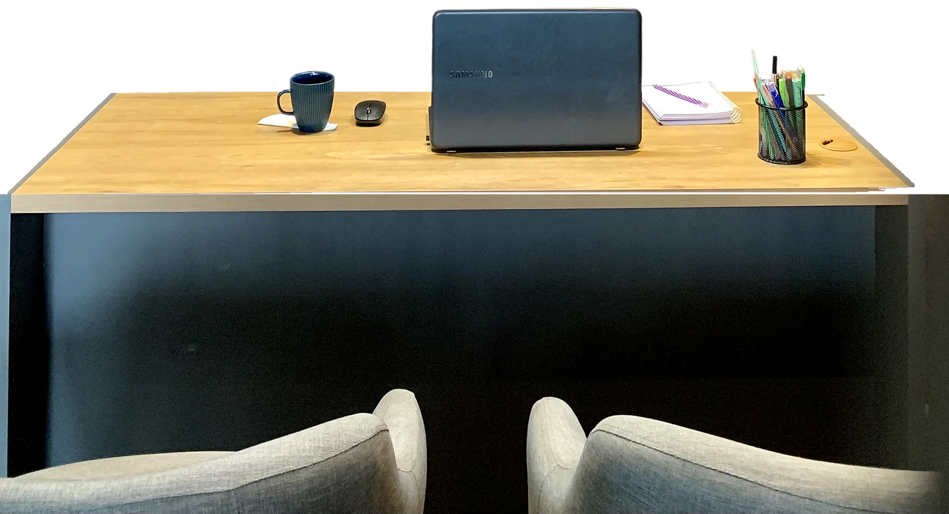 A mesa de conversa do consultório vista do lado do paciente: o tampo de carvalho com a caneca azul, o notebook, um caderno e o porta-canetas, e as duas poltronas cinza vazias em primeiro plano